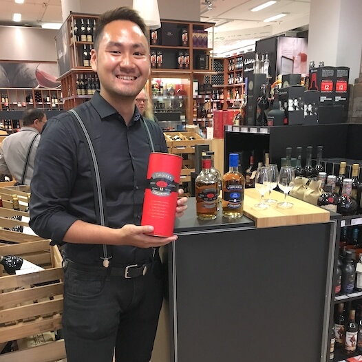 Promoter in schwarzer Kleidung präsentiert eine Whiskeyflasche im Rahmen einer Produktverkostung in einem Spirituosenladen