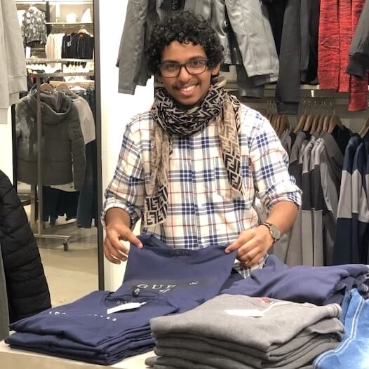 Verkäufer im Einzelhandel faltet Kleidung an einem Verkaufstisch in einem Modegeschäft